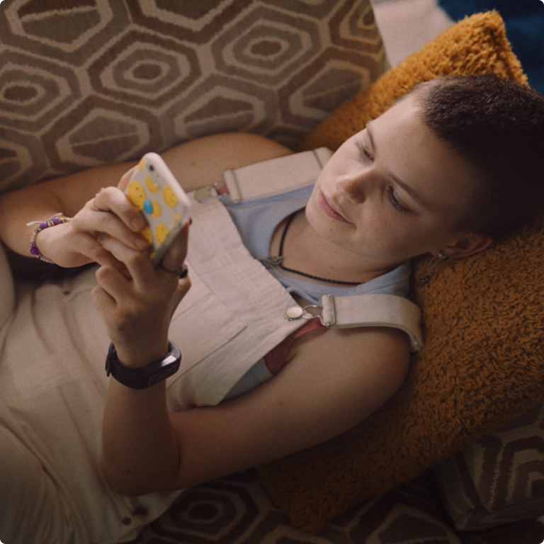Girl lying down on the sofa with her head on the pillow on her mobile phone