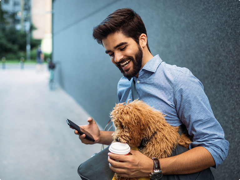 Man using his mobile phone while his dog tries to get a sip of his coffee