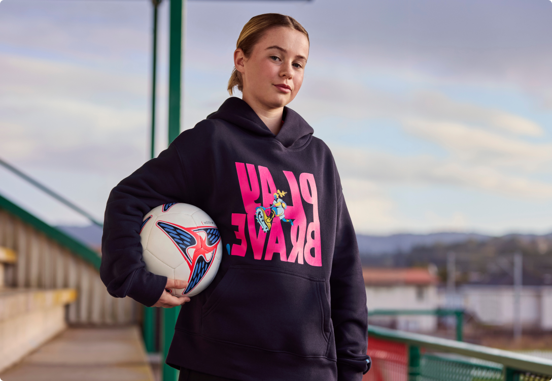 Young girl wearing the Play brave hoodie holding onto a football