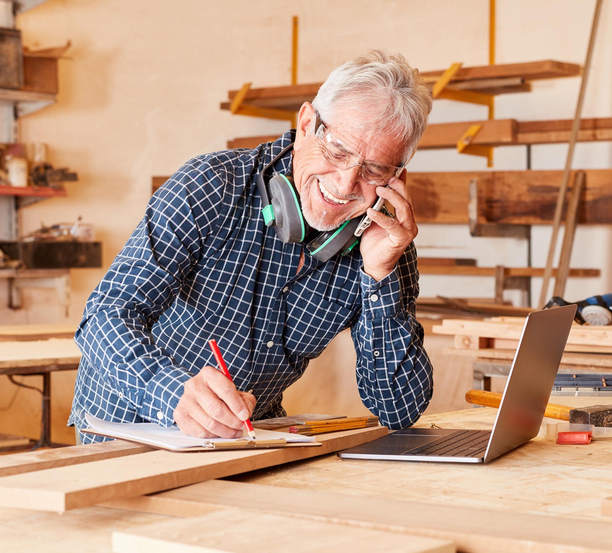 Man talking on his mobile phone and taking notes on a clipboard in a workshop