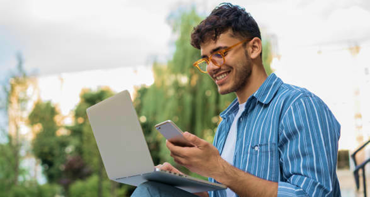 Man sitting outside working on his laptop and looking at his mobile phone